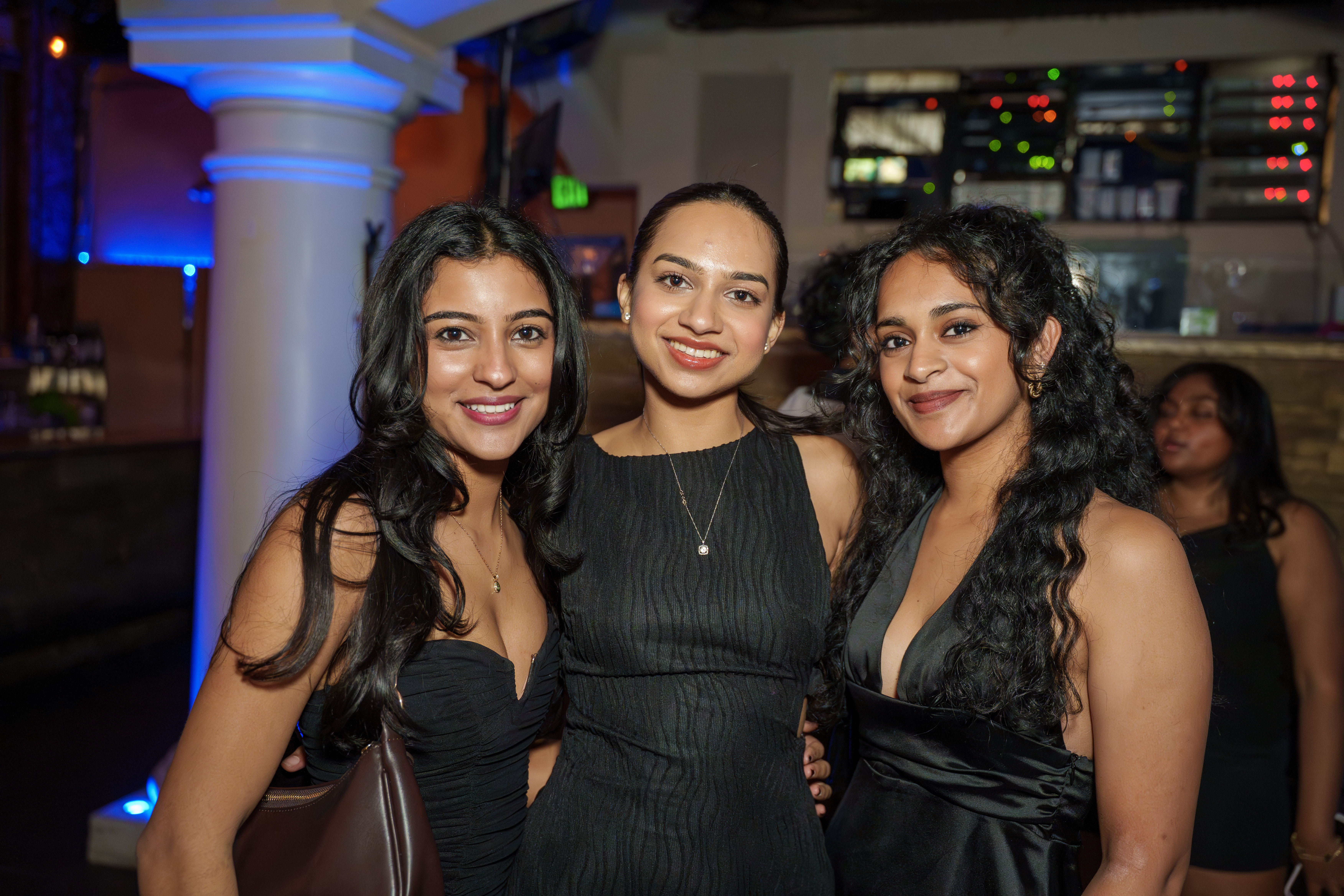 Three friends posing together in black outfits at a nightclub