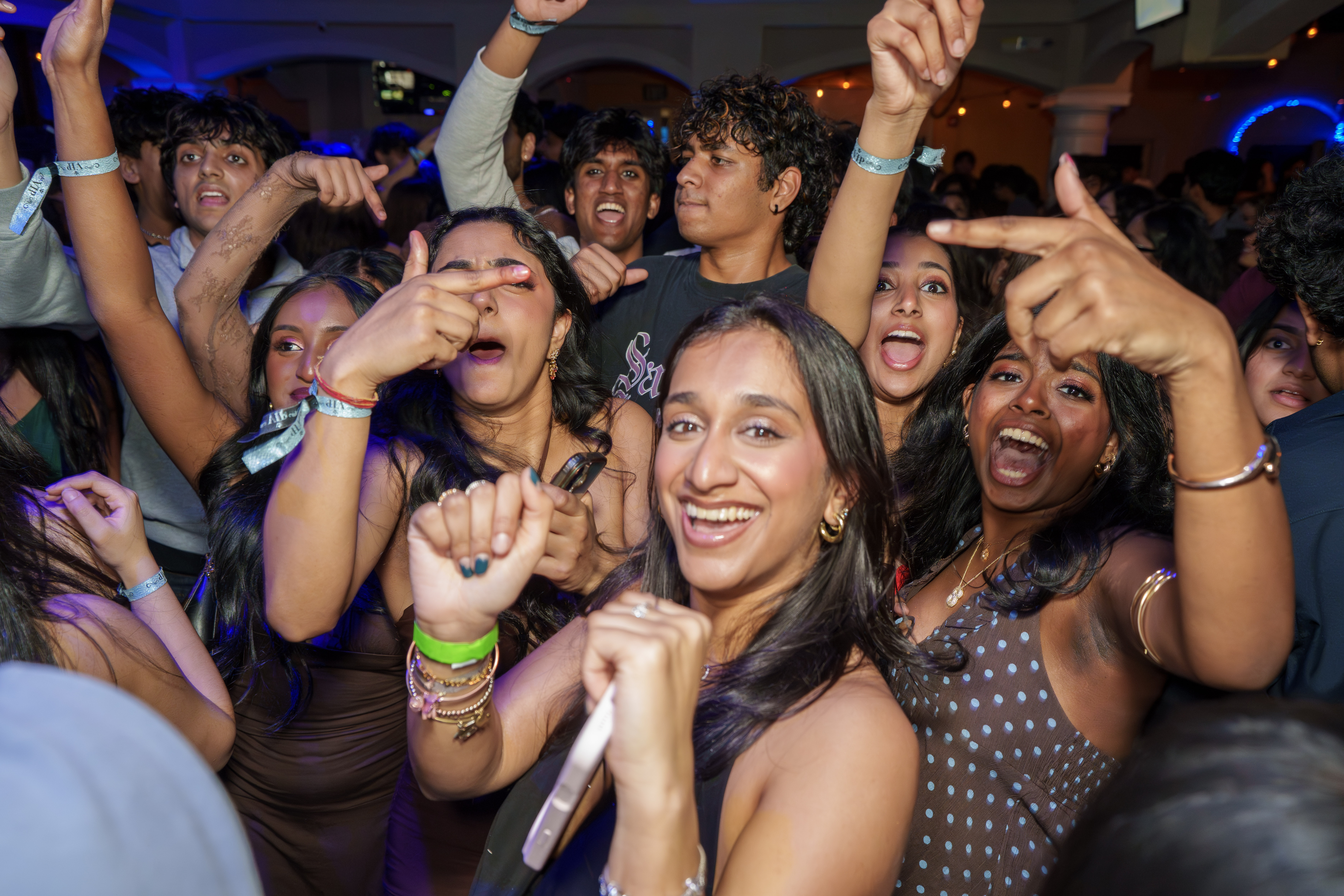 Crowd cheering and dancing together beneath blue club lights