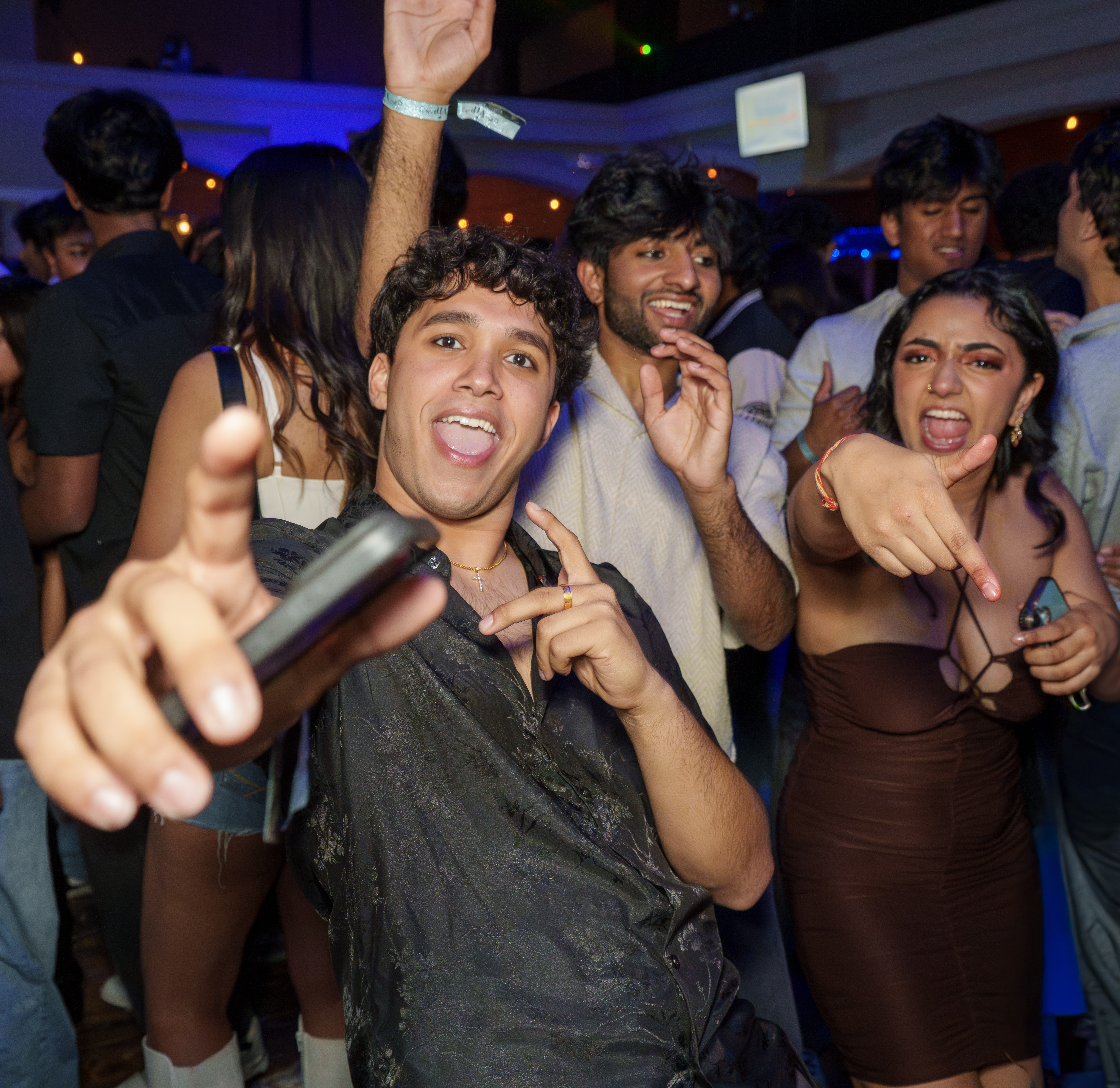 Friends pointing toward the camera while dancing at a crowded party