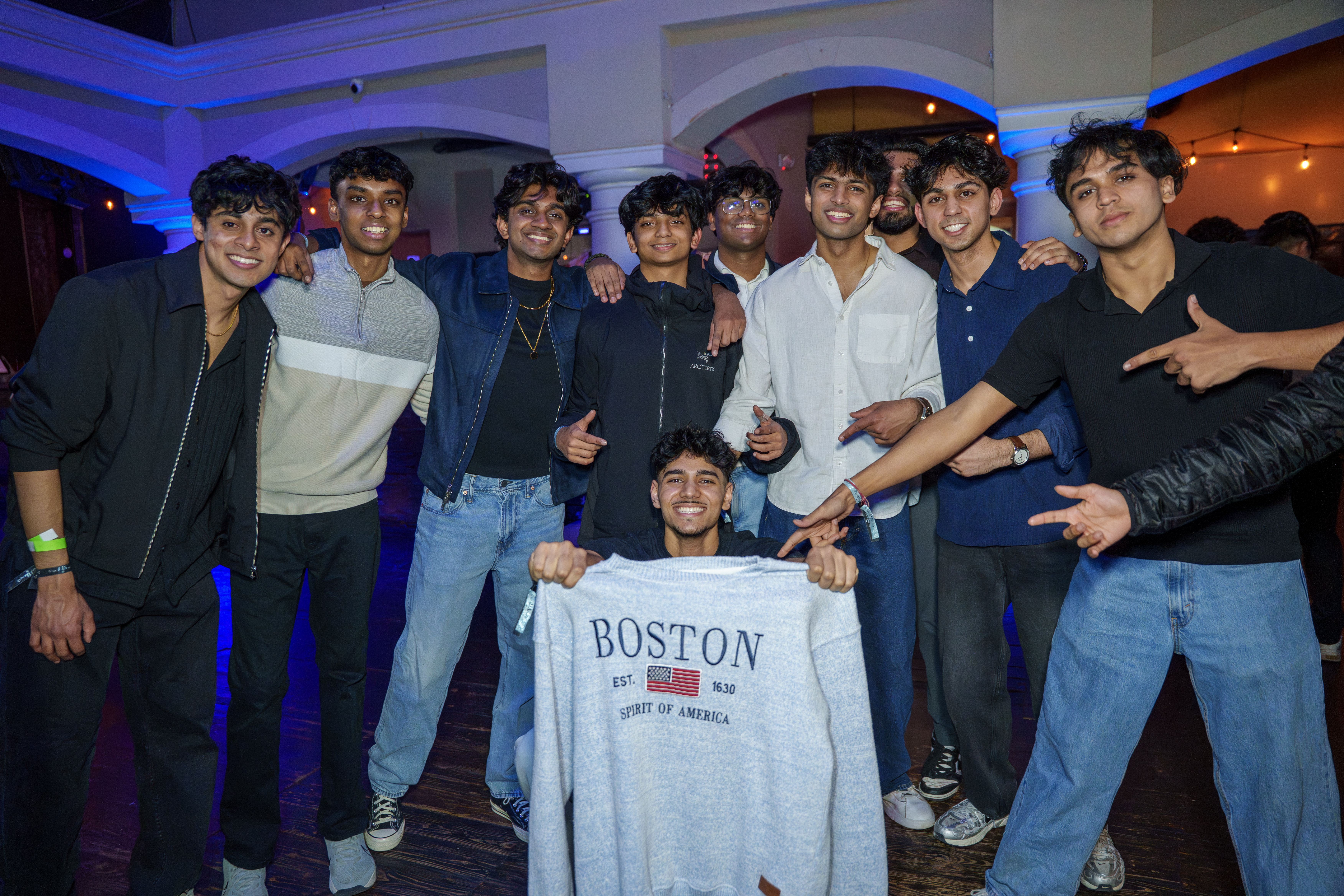 Group of friends posing together with a Boston sweatshirt at a party
