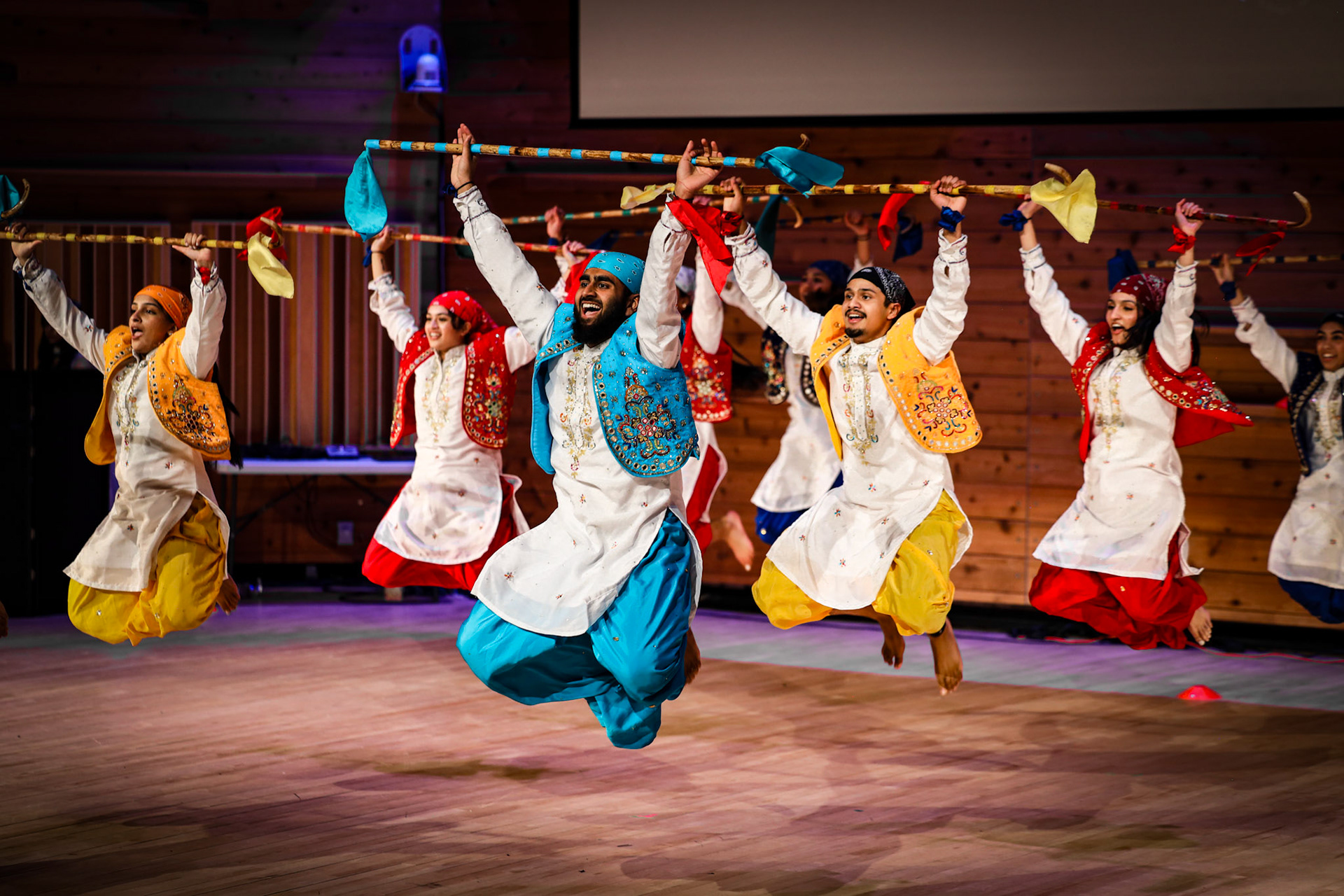 Bhangra dancers leaping with colorful staffs during a stage performance