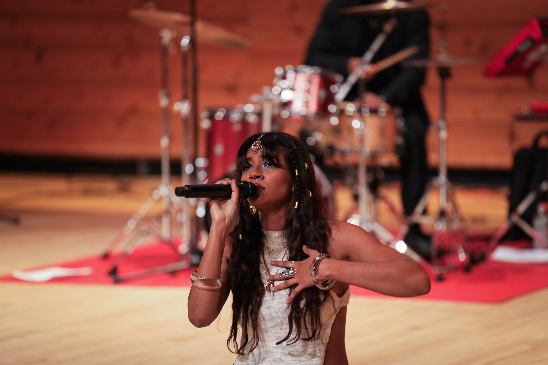 Vocalist singing in front of a live drum kit during a cultural showcase