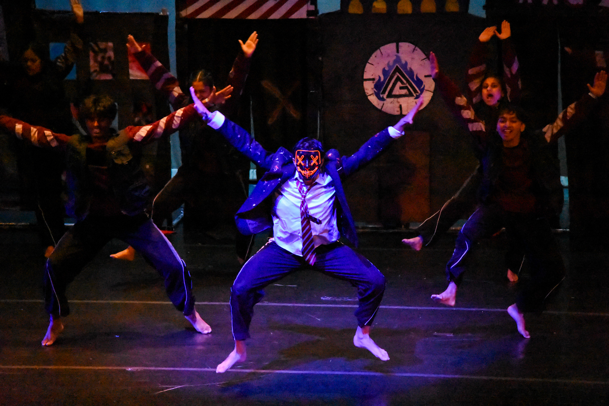Masked lead dancer and ensemble performing under dramatic stage lighting