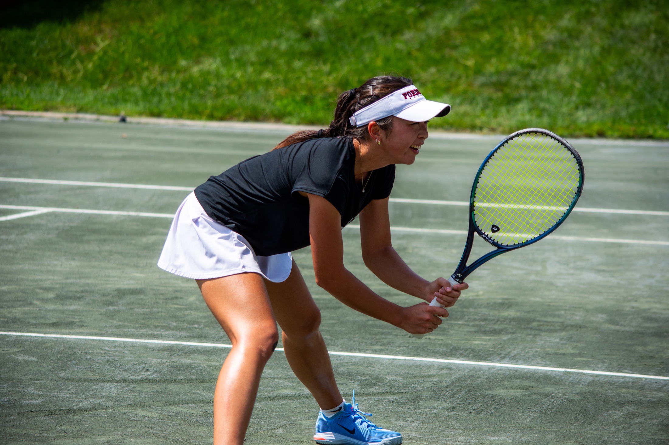 Tennis player in black settling into a ready position at the baseline