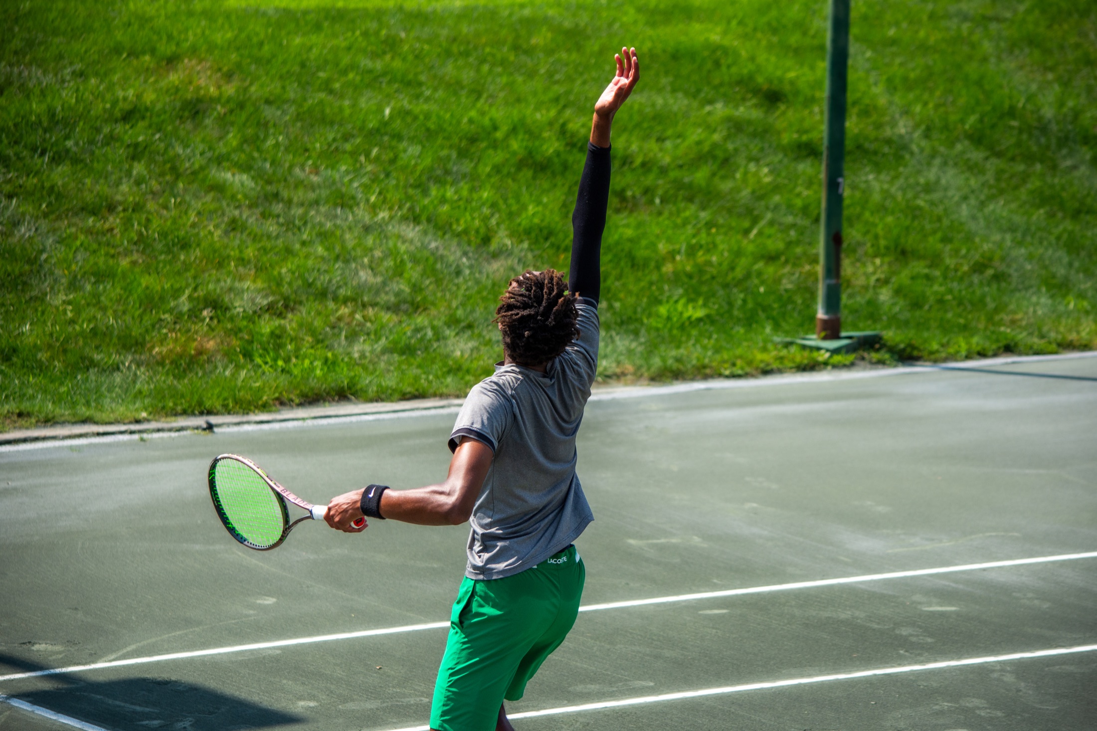 Tennis player in green extending upward through a powerful serve