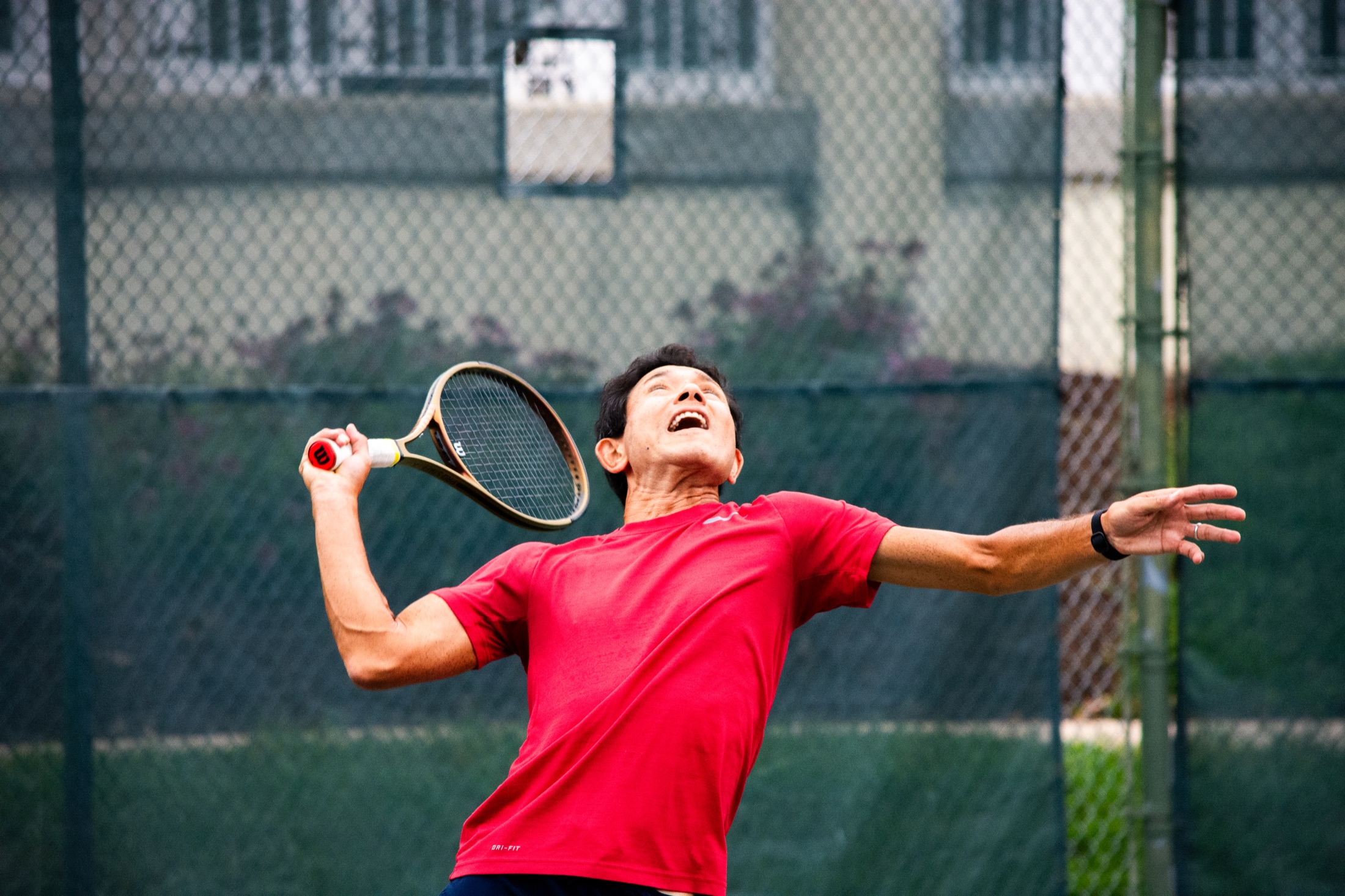 Tennis player in red tracking the ball for an overhead shot