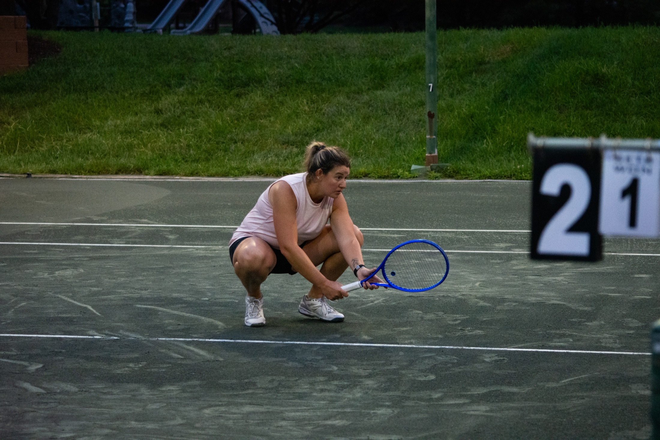 Tennis player in pink crouching at the baseline beside the scoreboard