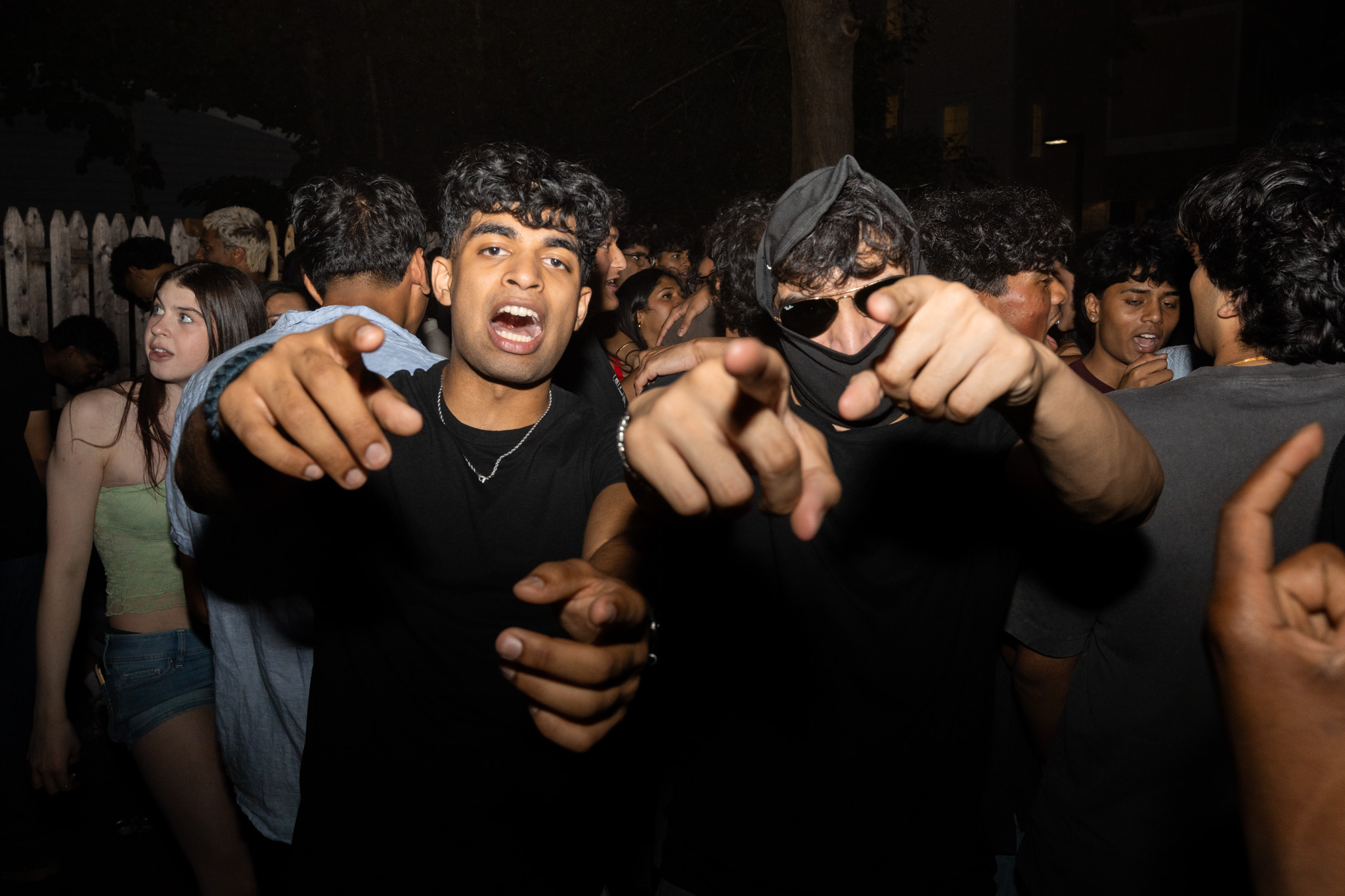 Friends pointing toward the camera in a crowded backyard graduation party
