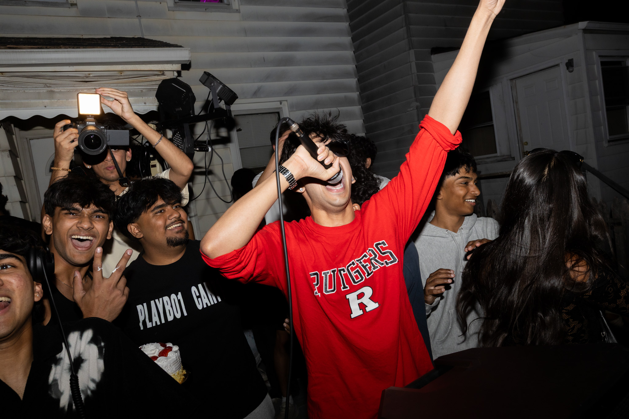 Singer in a red Rutgers shirt performing at an outdoor graduation party