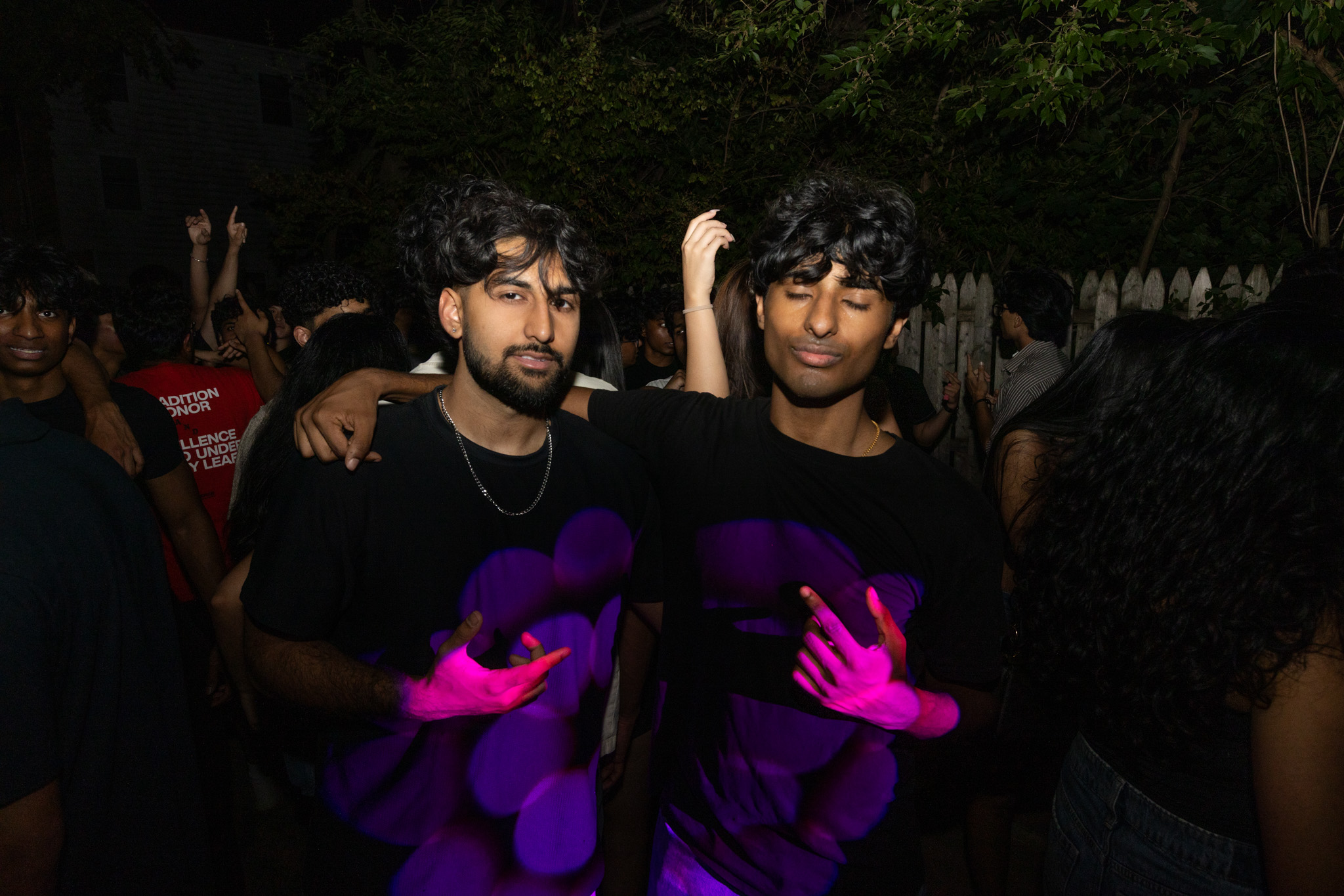 Two friends posing under purple lighting at an outdoor graduation party