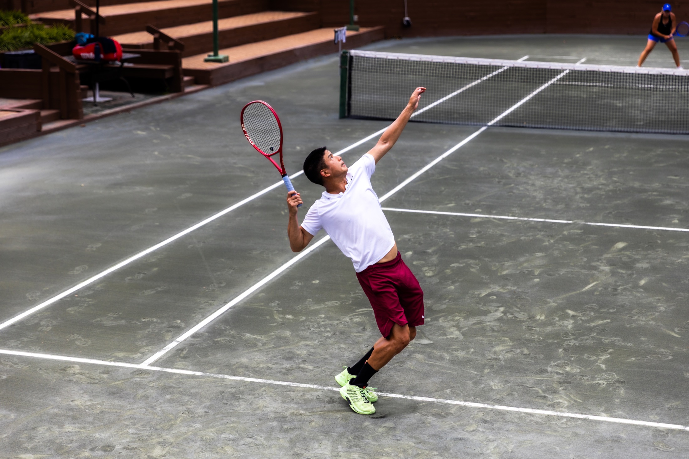 Tennis player in white launching into a serve on the tournament court